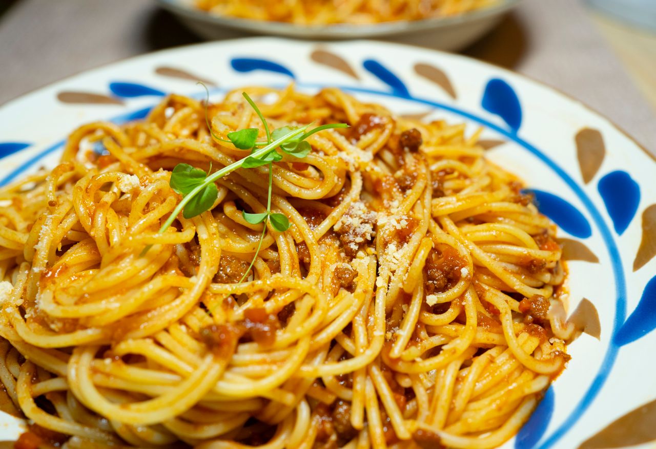 heros-img Close-up of savory spaghetti Bolognese garnished with fresh herbs on a decorative plate.