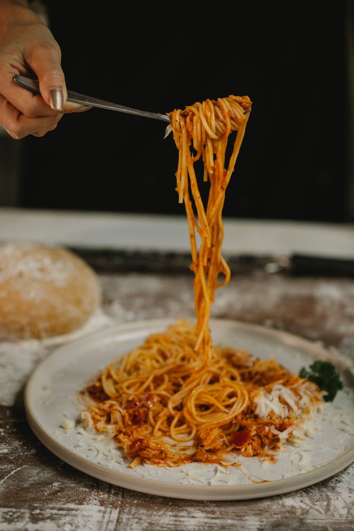 about-us-02 Crop anonymous female with fork enjoying freshly cooked spaghetti with tomato sauce served on white ceramic plate